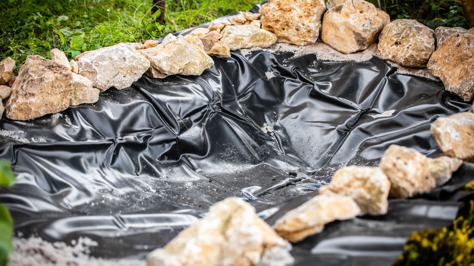 A close-up shot of a black colored liner on a dugout hole in a yard area, all situated in a well lit area outdoors