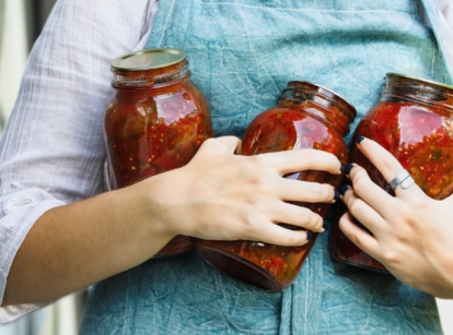 A person holding jars of salsa using crops of a salsa garden while the person wore a blue apron