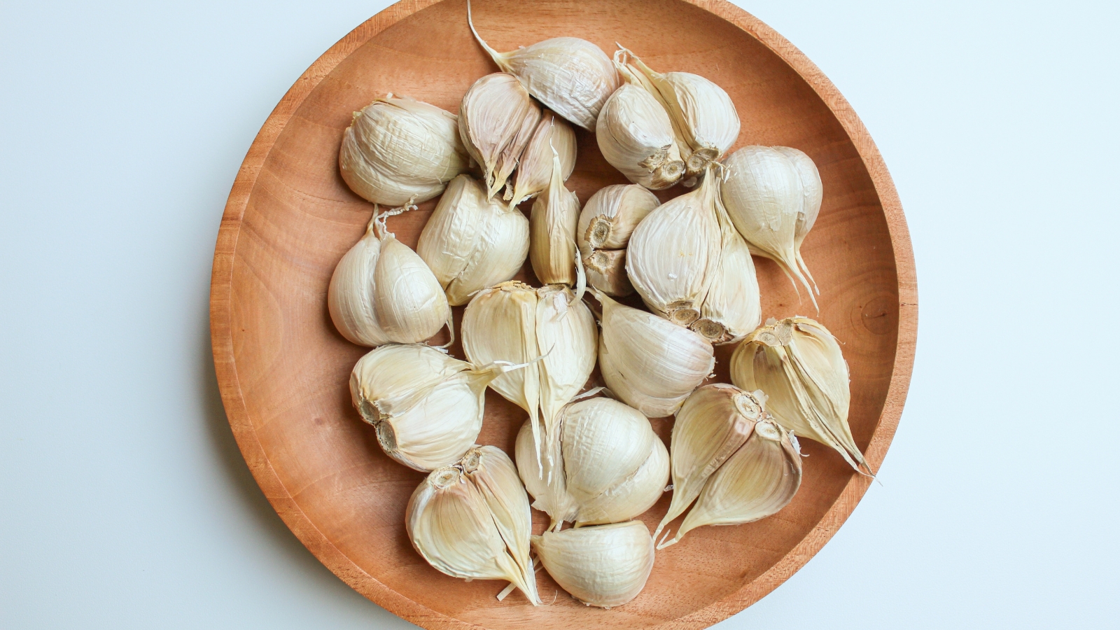 A round wooden plate holds numerous white, papery-wrapped bulbs, each with a dry, crinkled exterior, against a soft, light background.
