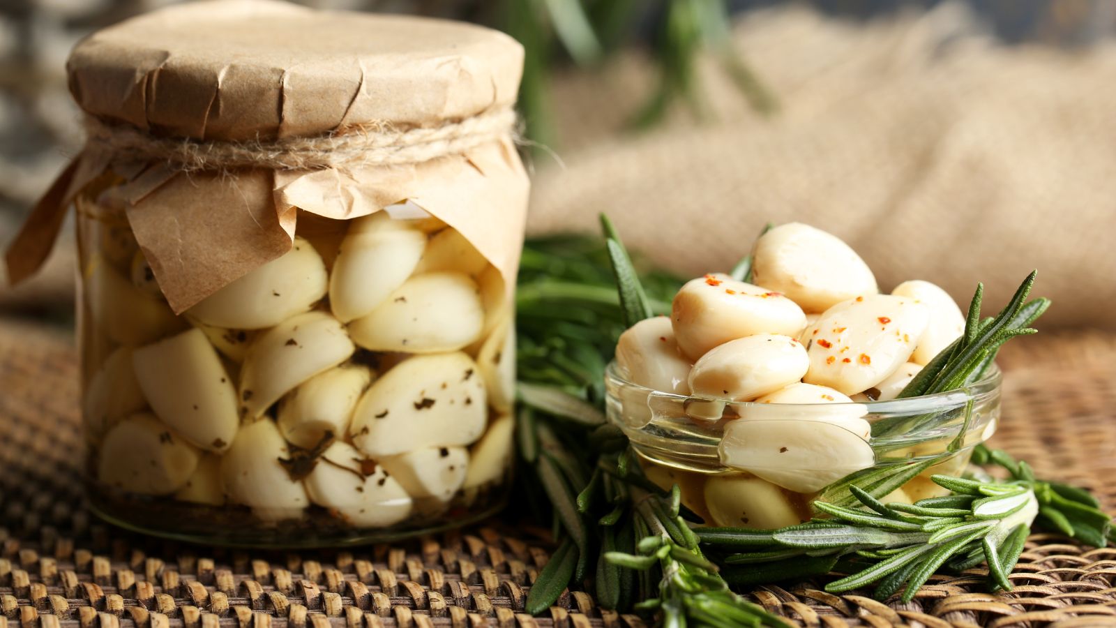 Allium sativum placed in a jar to preserve it on a woven mat with herbs beside the bulb's continers