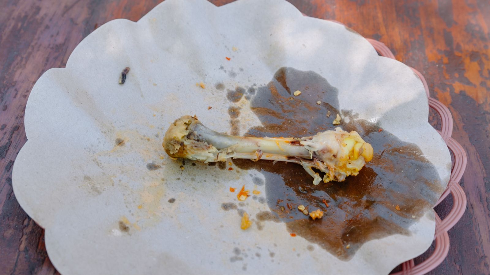 A close-up and overhead shot of a bone food scrap on an oily paper-lined plate, situated in a well lit area indoors