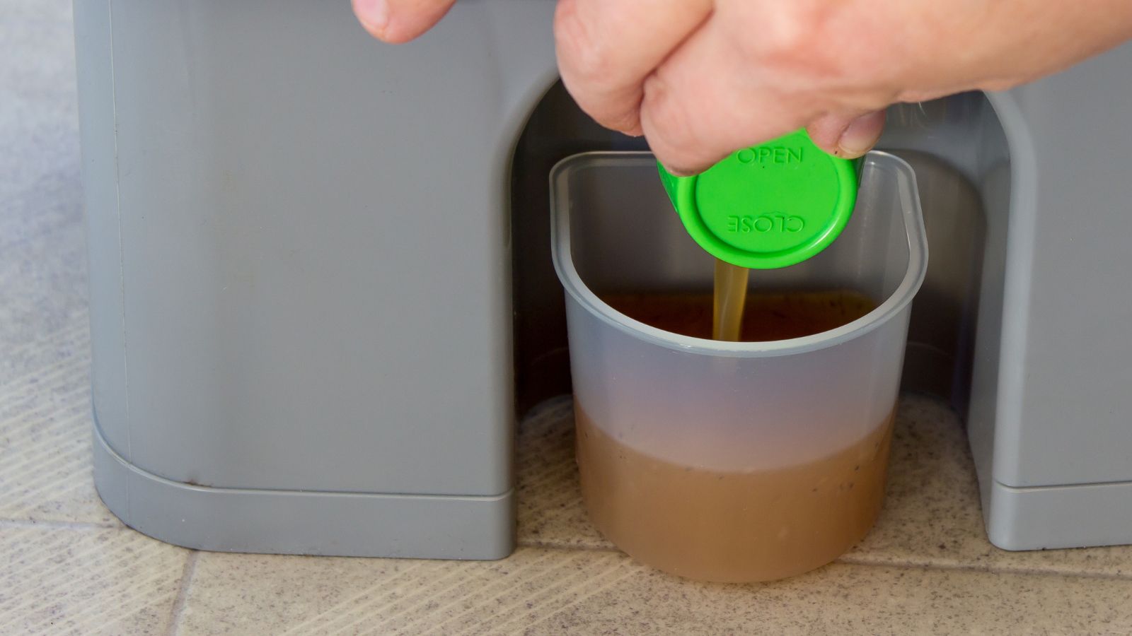 A close-up shot of a person in the process of extracting liquid from a compost bin in a well lit area indoors