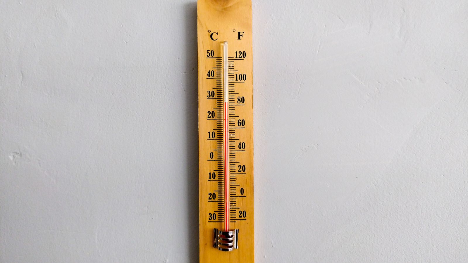 A wooden thermometer on a gray wall appearing to have a red line in the middle inside a glass tube held by a metal fitting