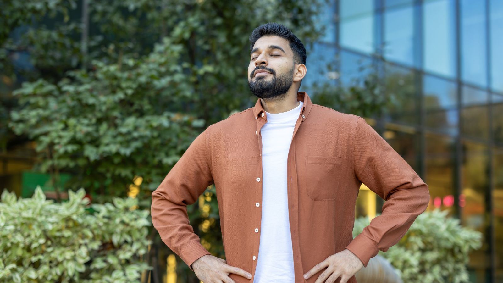 A close-up shot of a person in an urban commercial area with trees and plants breathing in air outdoors