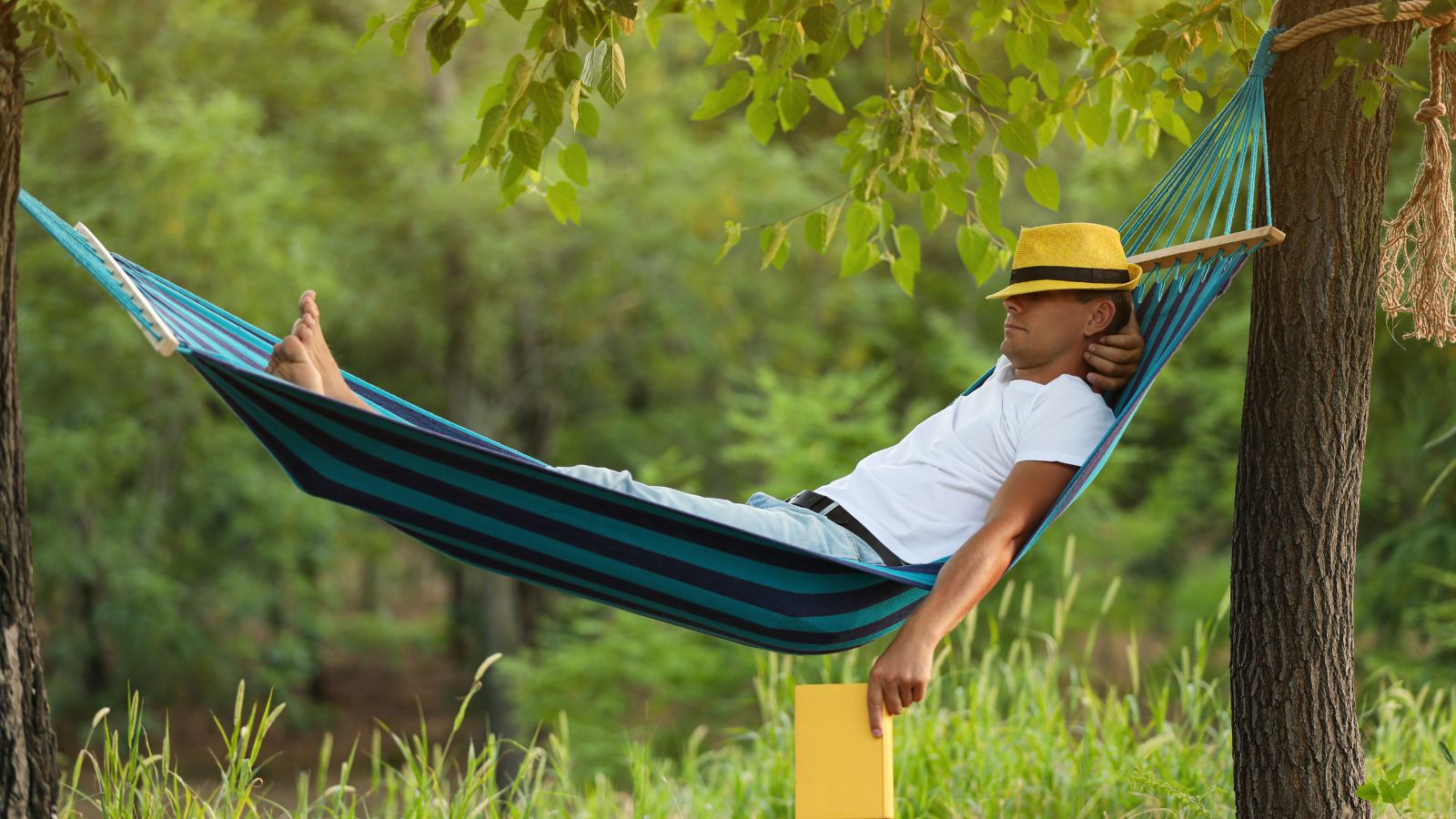 A close-up shot of a person sleeping in a hammock placed near a tree forest outdoors