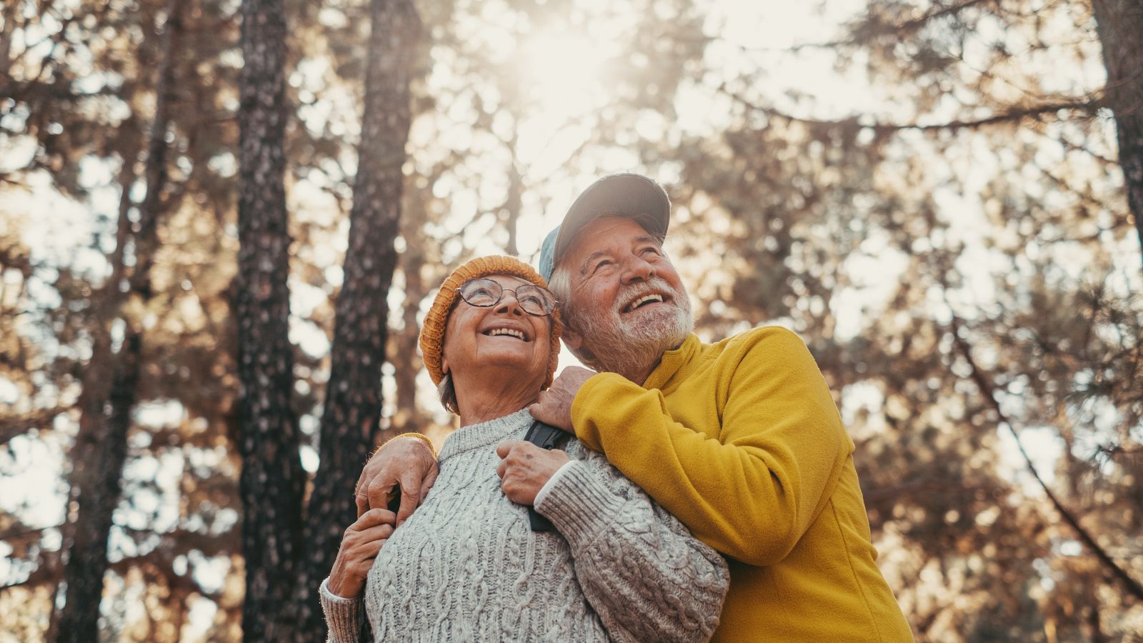 A close-up shot of a very happy elderly couple in a tree forest area, surrounded by warm sunlight peeking through leaves