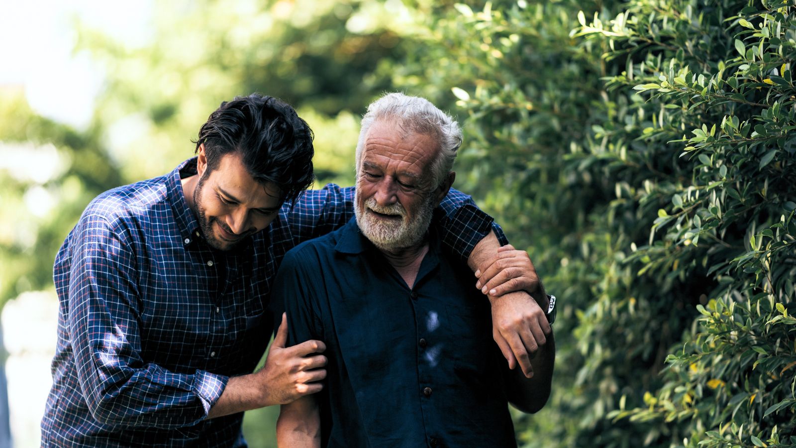A shot of a father and his son walking on a pathway with a large composition of trees in the background