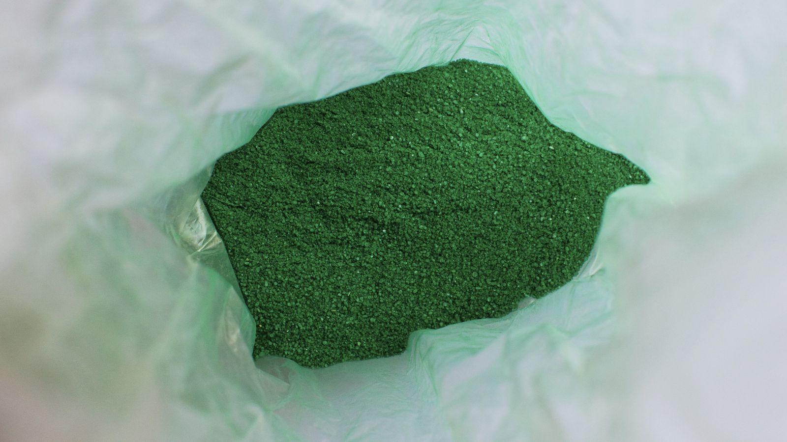 An overhead and close-up shot of a green colored soil amendment, all placed in a large plastic bag in a well lit area
