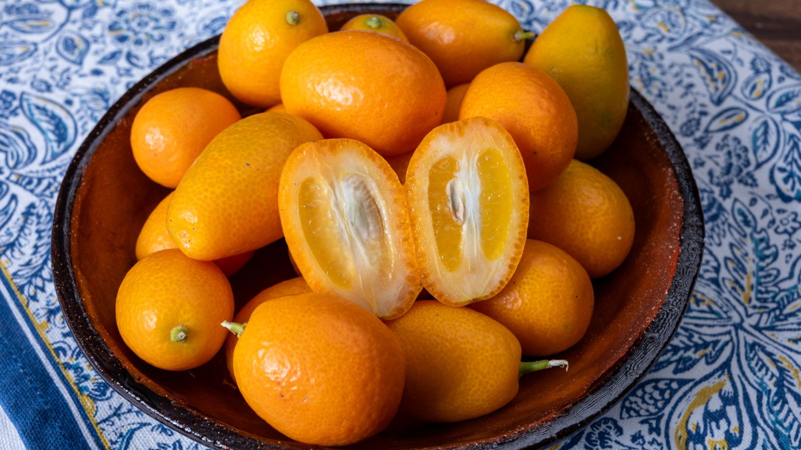 A shot of several freshly harvested orange, oval fruits placed on a bowl in a well lit area indoors