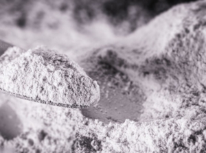 A pile of white dust made of rock phosphate meant to be fertilizer being scooped by a metal scooper
