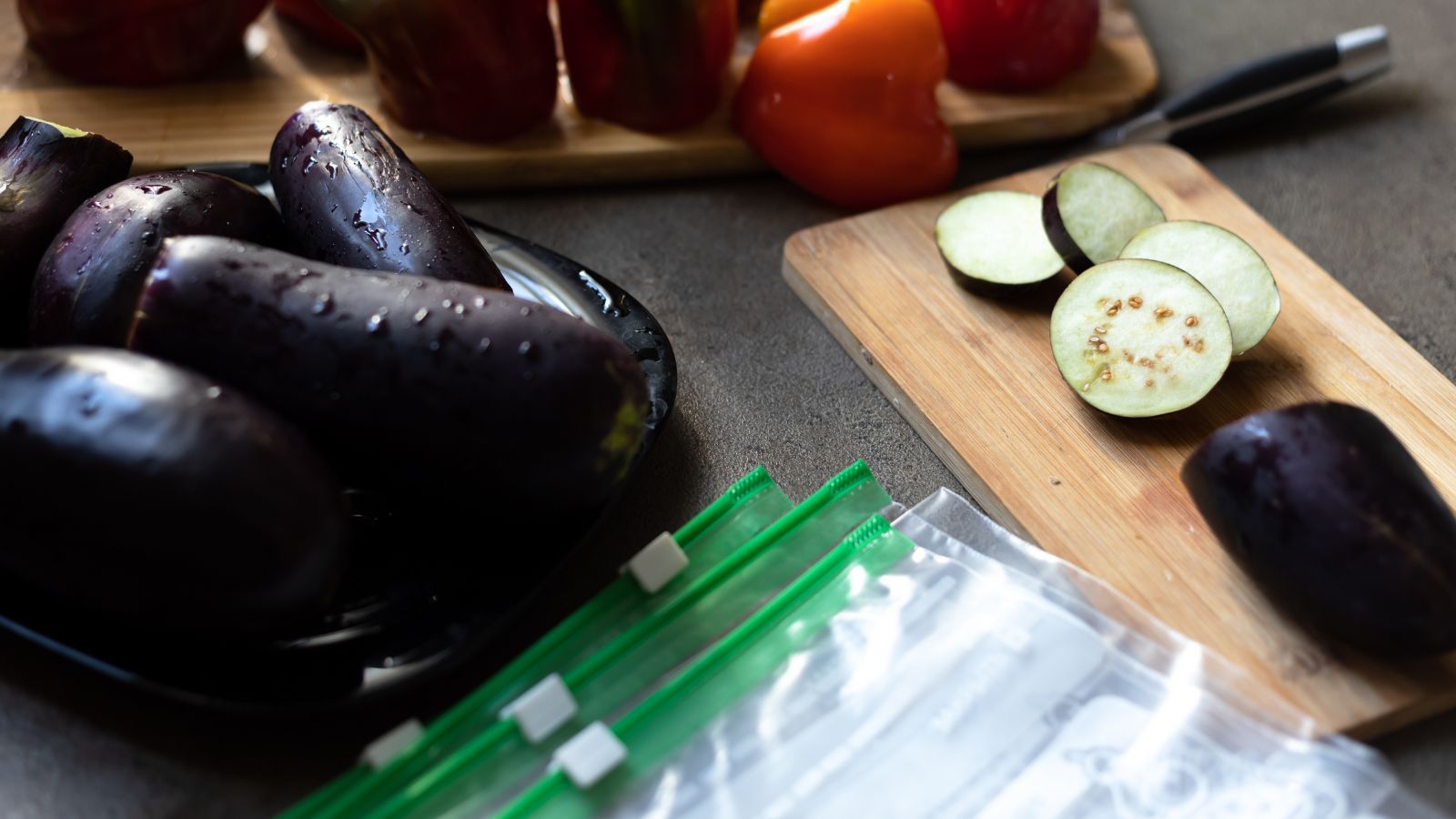 A shot of freshly harvested purple crops alongside other crops, being sliced on a chopping board with plastic bags on the side, all situated in an area indoors