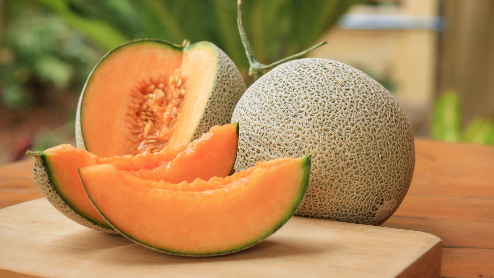 A shot of sliced round melon fruits placed on a chopping board on top of a wooden table.