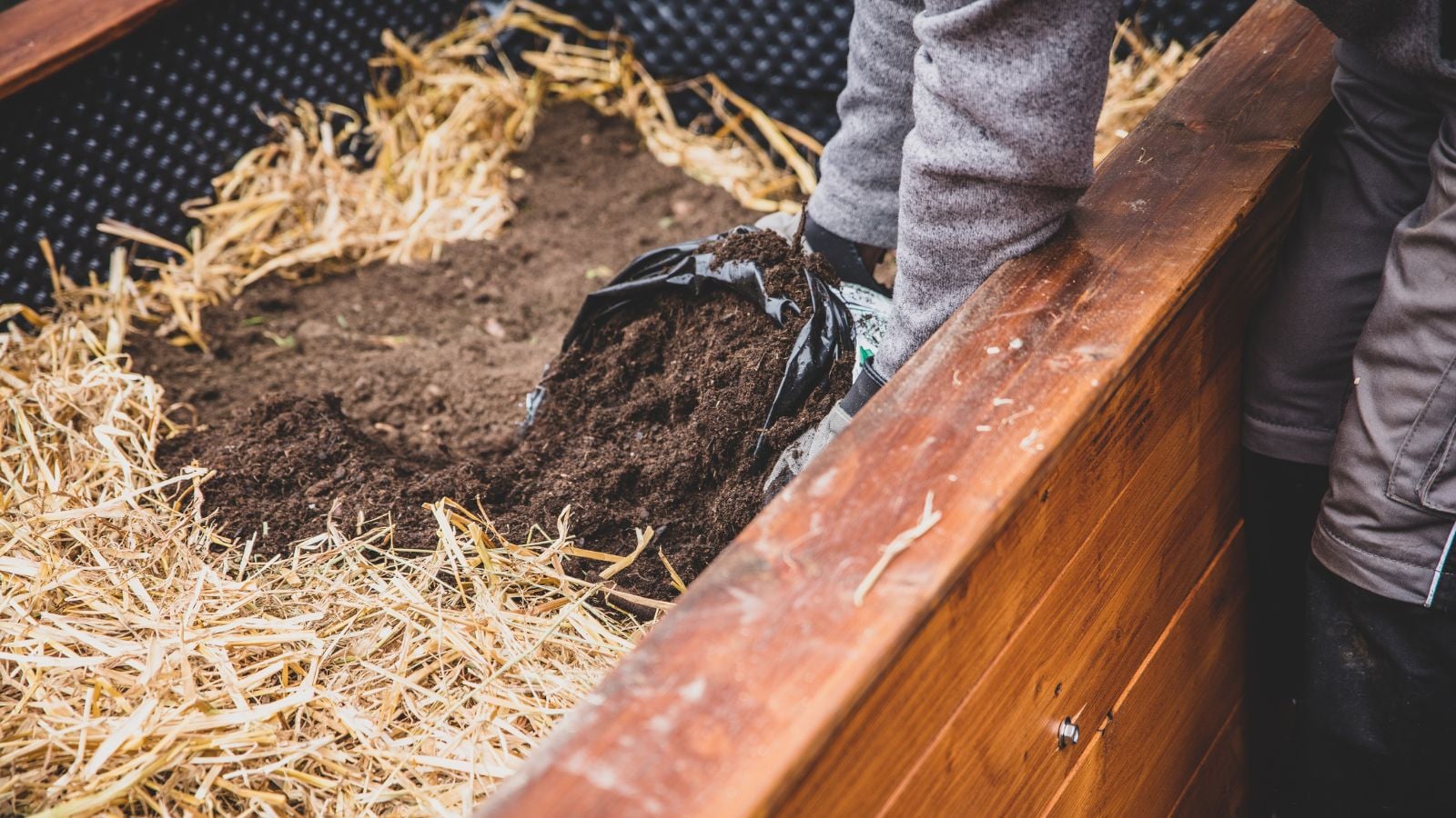 A close-up shot of a person in the process of filling a large planter with mulch and several other soil amendments