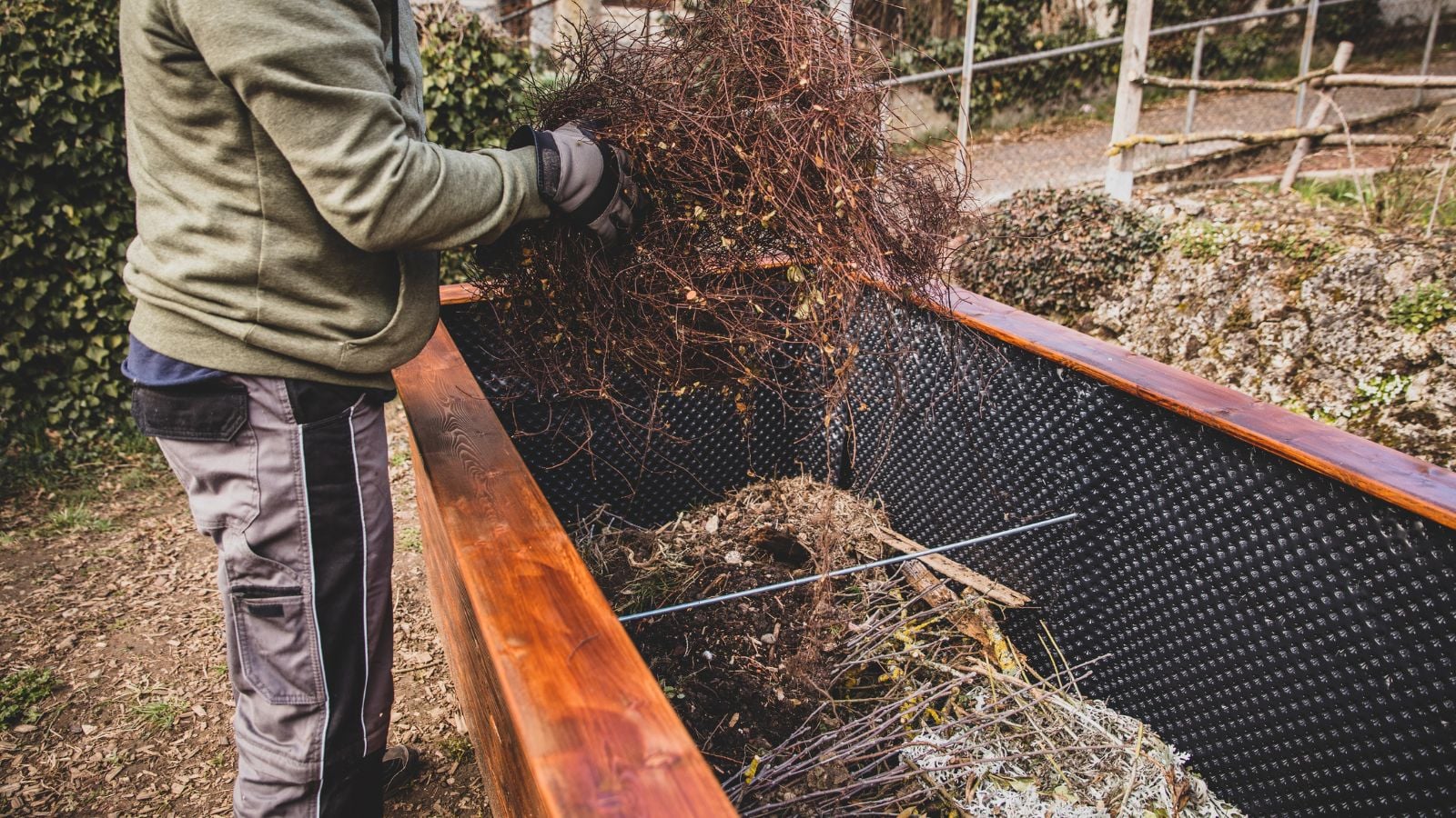 A close-up shot of a person in the process of filling up a newly built planter, showcasing the hugelkultur raised bed