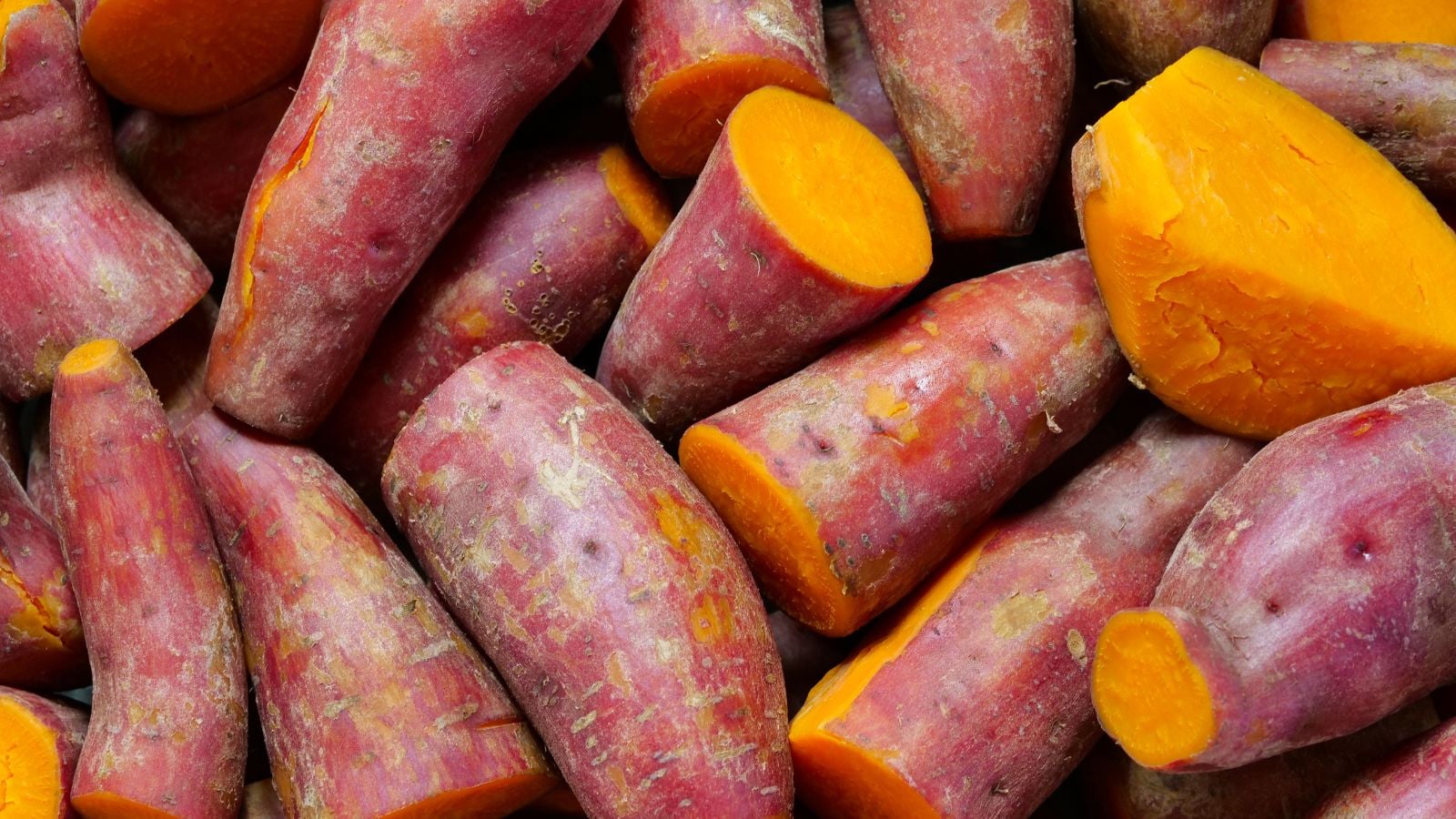 An overhead and close-up shot of a small composition of Bayou Belle variety of crops, showcasing garnet colored skin and orange flesh
