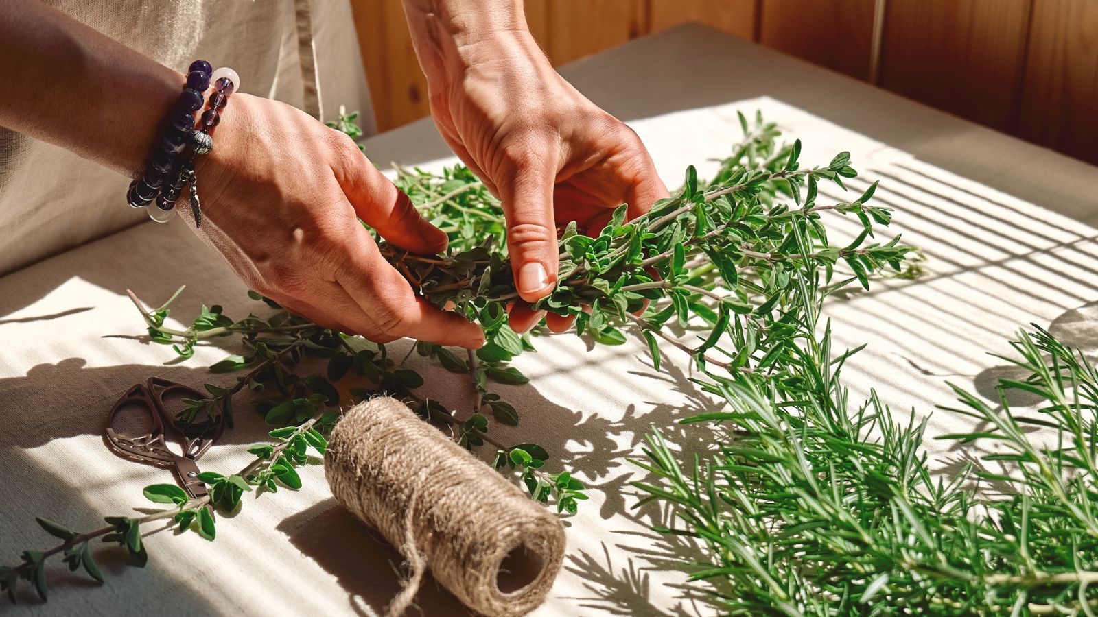 A close-up shot of a person in the process of tying herbs using a twine, preparing them for hang drying, all situated in a well lit area indoors