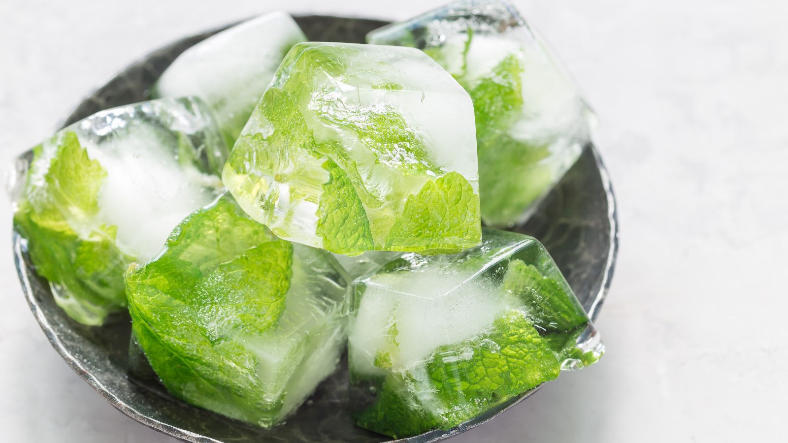 A shot of ice cubes with frozen leaves of an herb placed on a black plate
