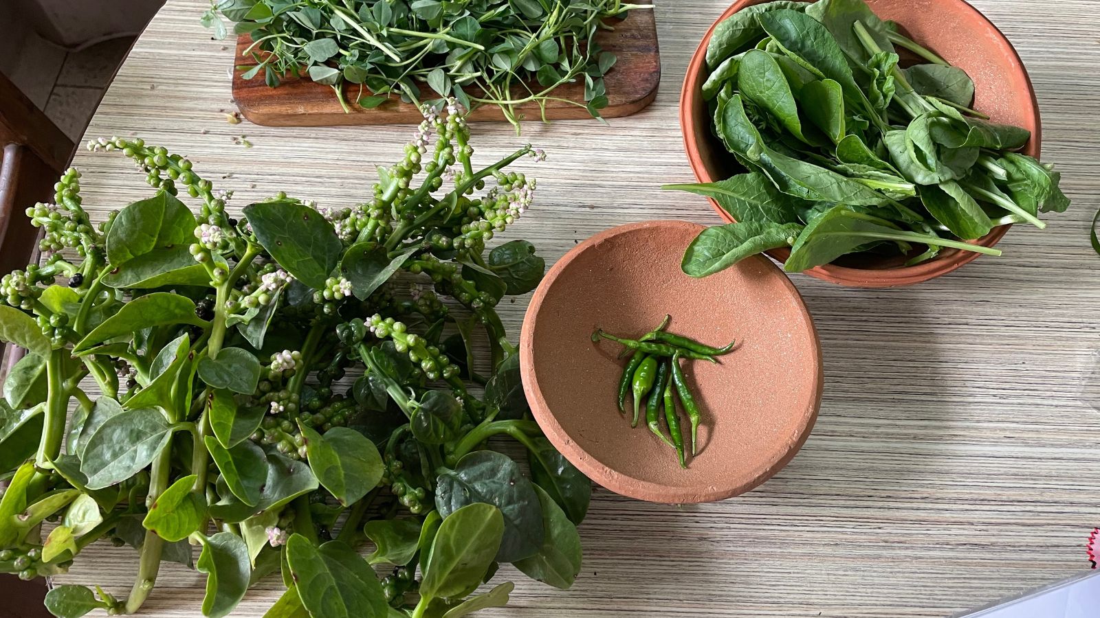 An overhead flat lay shot of several leafy vining greens placed on separate containers, all placed on a wooden table indoors