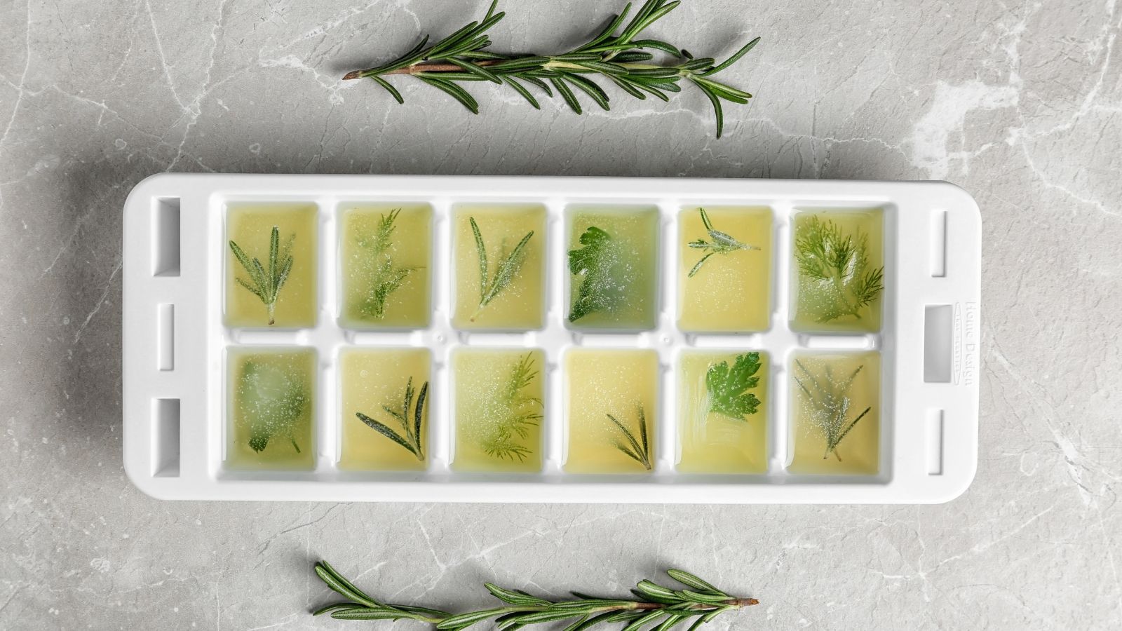 An overhead shot of an ice cube tray with several frozen herbs