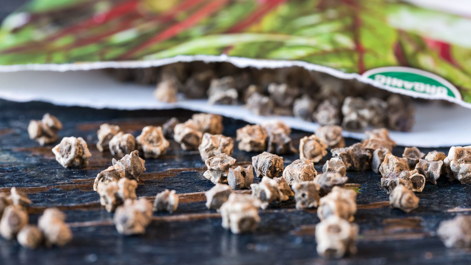 A close-up shot of a composition of scattered plant ovules from a packet, all placed on a black surface indoors