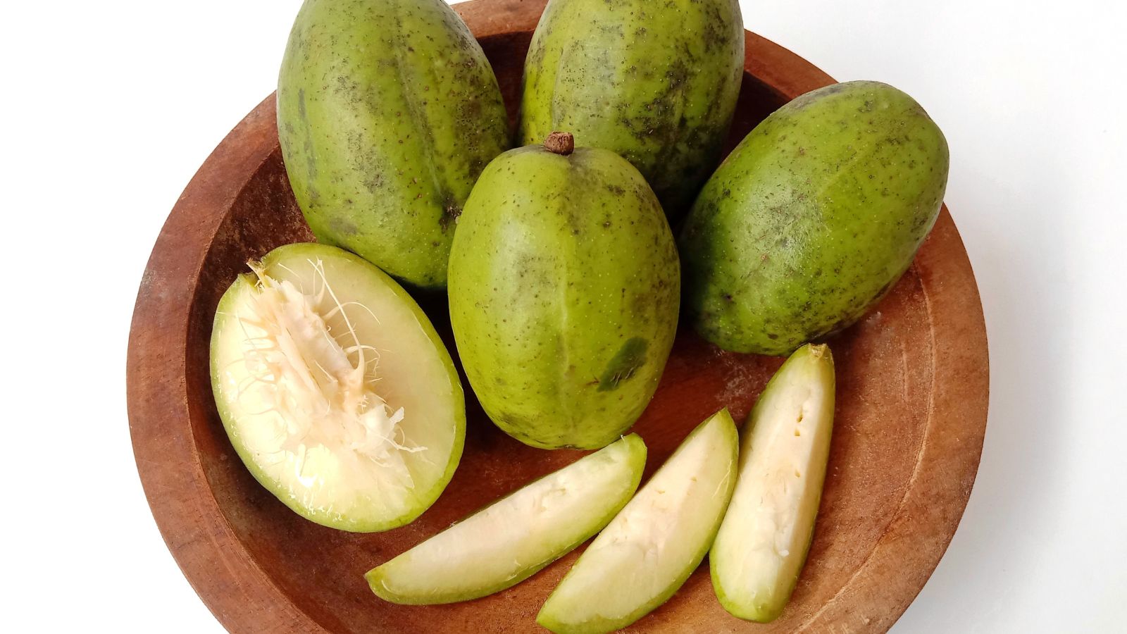 An overhead shot of fruits of a large plant that is placed in a wooden bowl in a well lit area