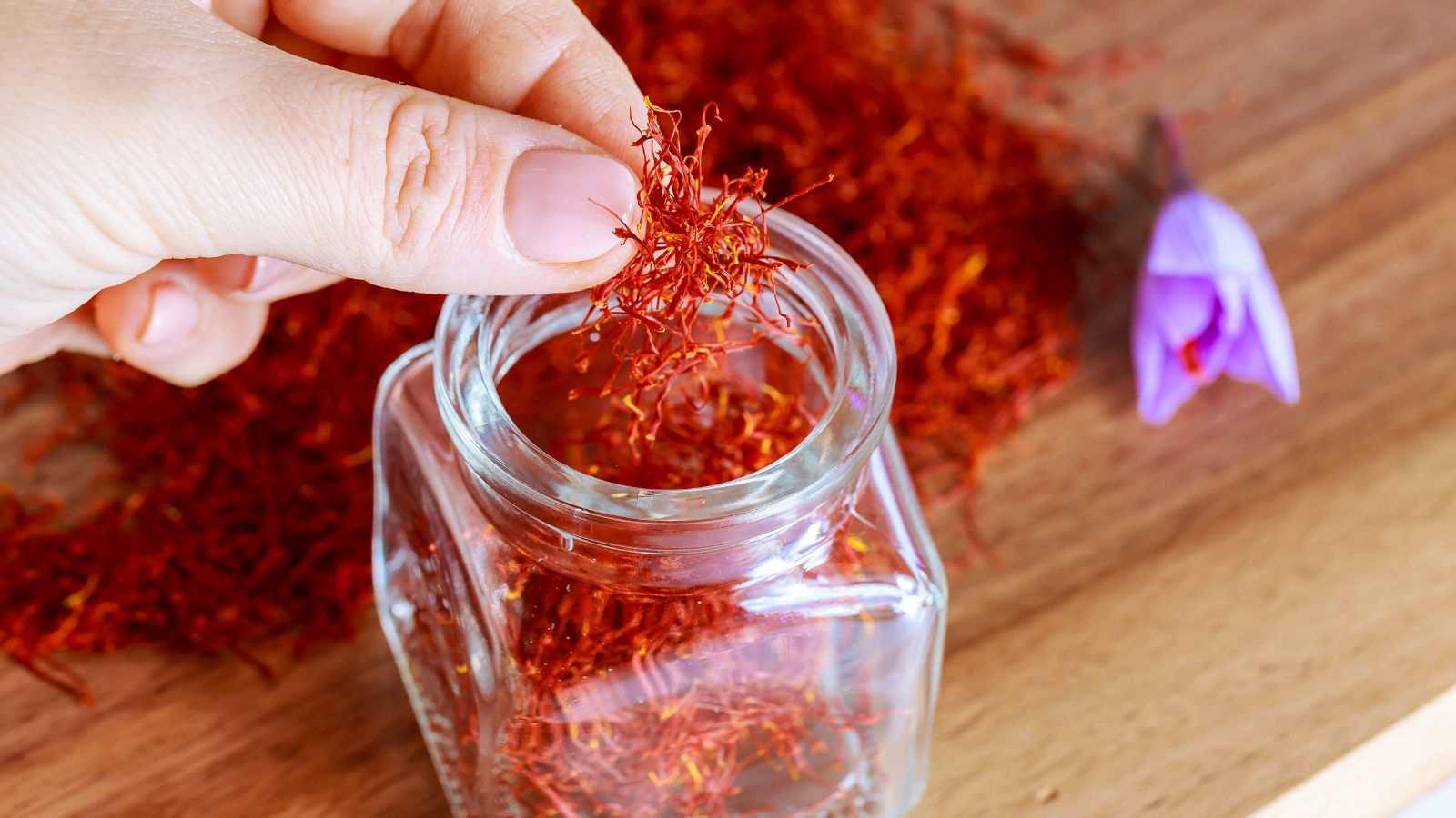 A close-up shot of a person in the process of placing red colored threads of a spice plant in a jar, all situated in a well lit area indoors