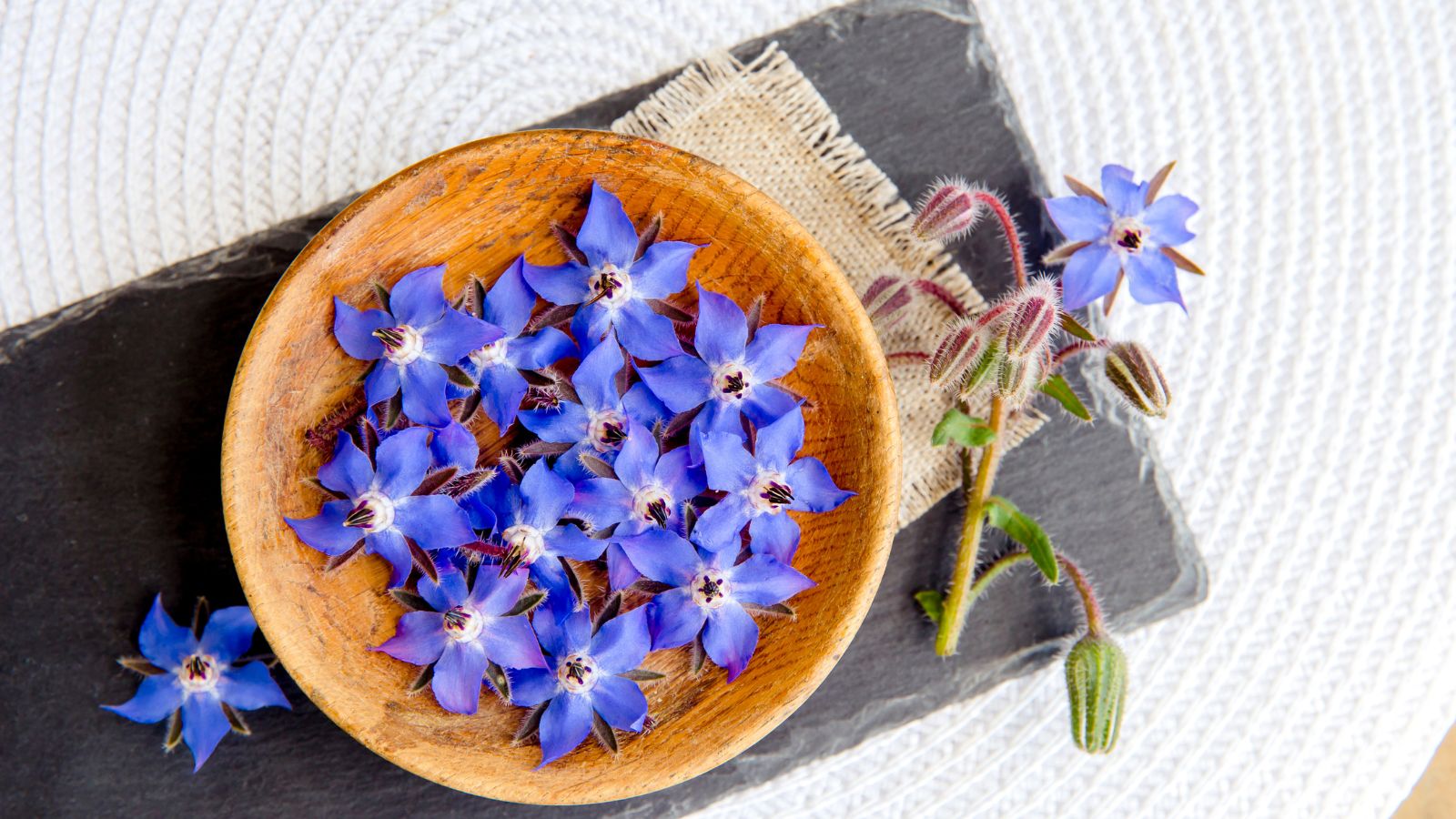 An overhead shot of harvested blue flowers and leaves of a plant placed on a wooden plate