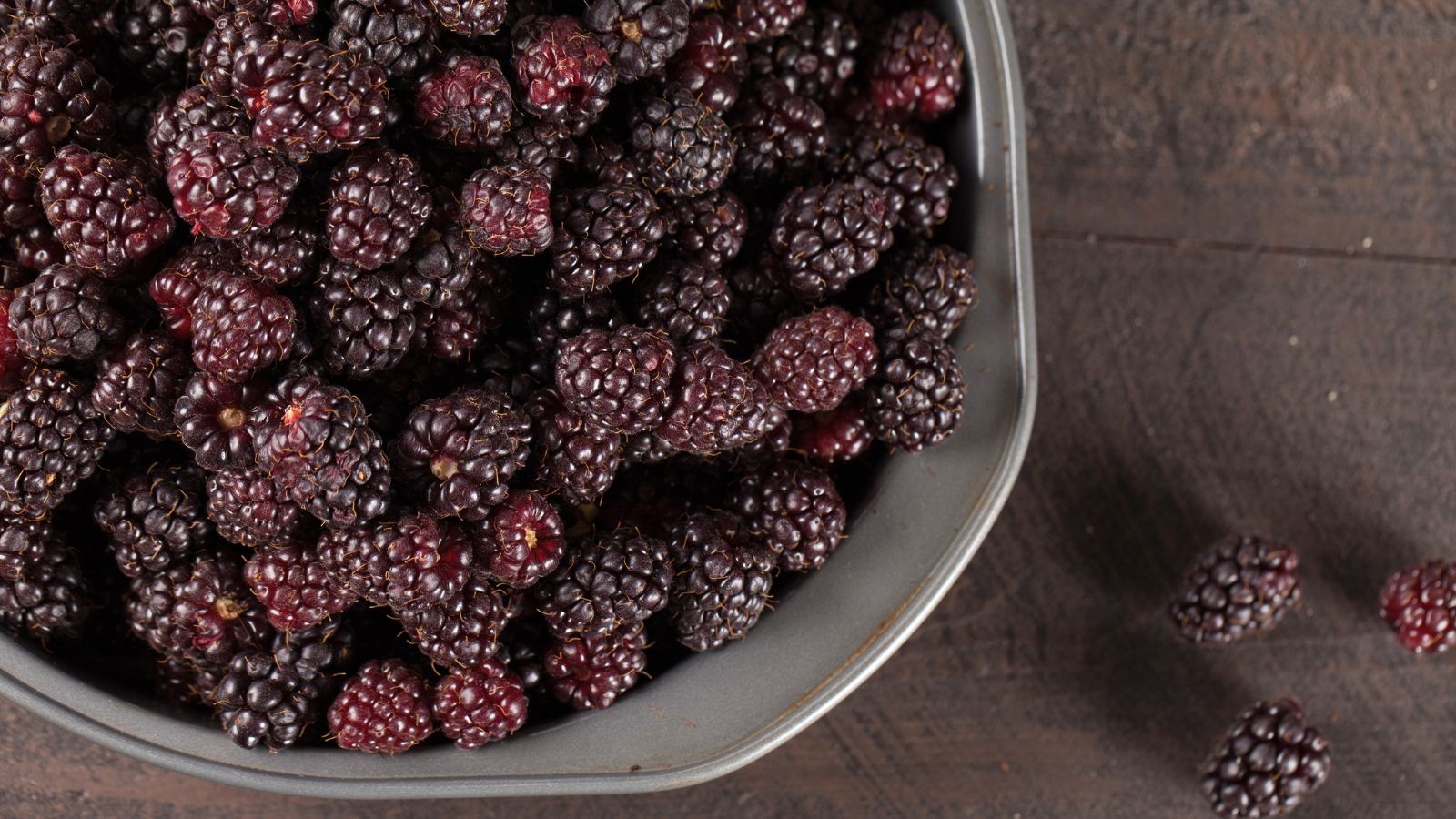 An overhead shot of freshly harvested fruits that is placed in a bowl on a wooden surface