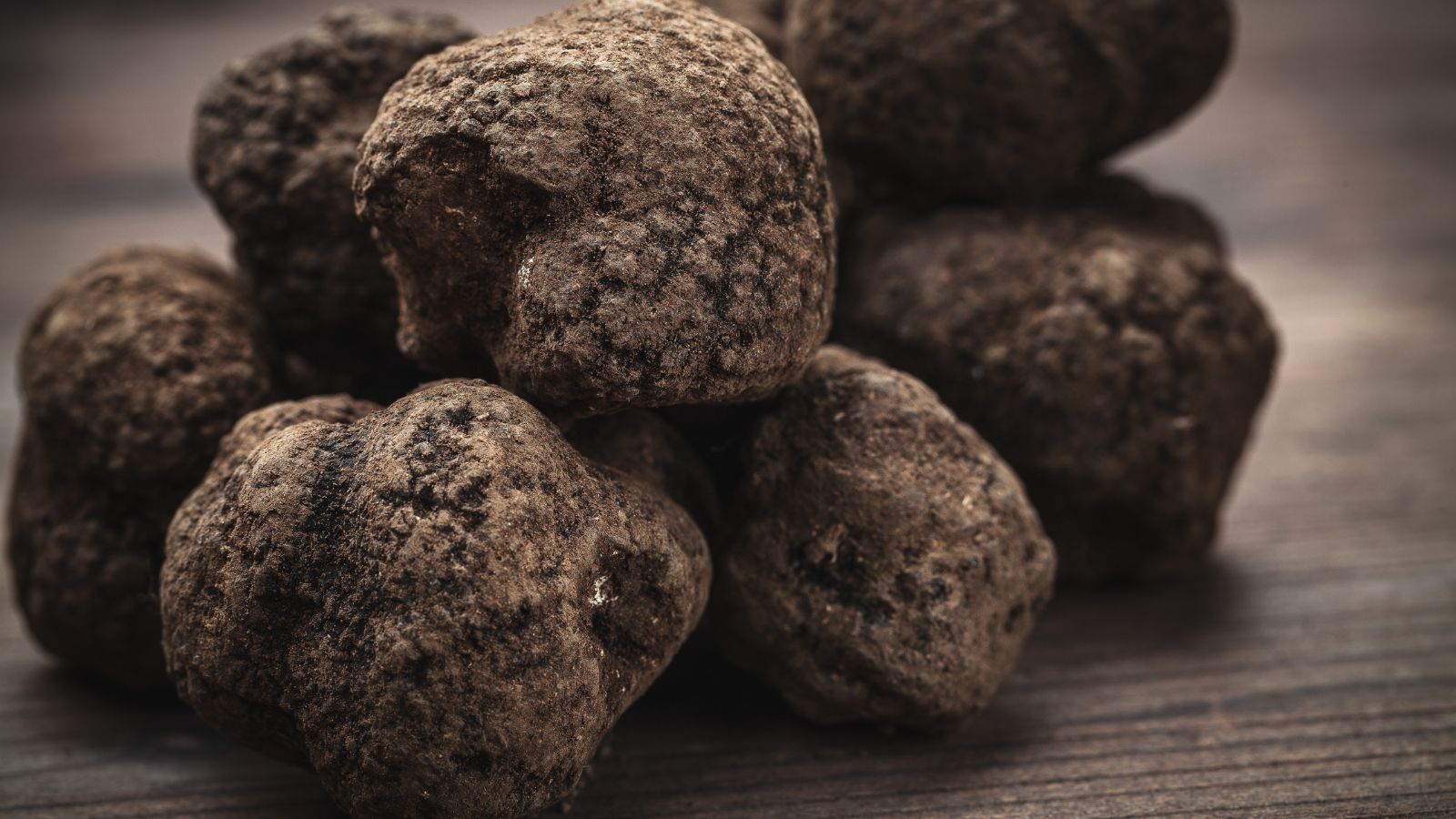 A pile of dark brown Tuber melanosporum placed on a dark wooden surface, appearing to be placed somewhere shady
