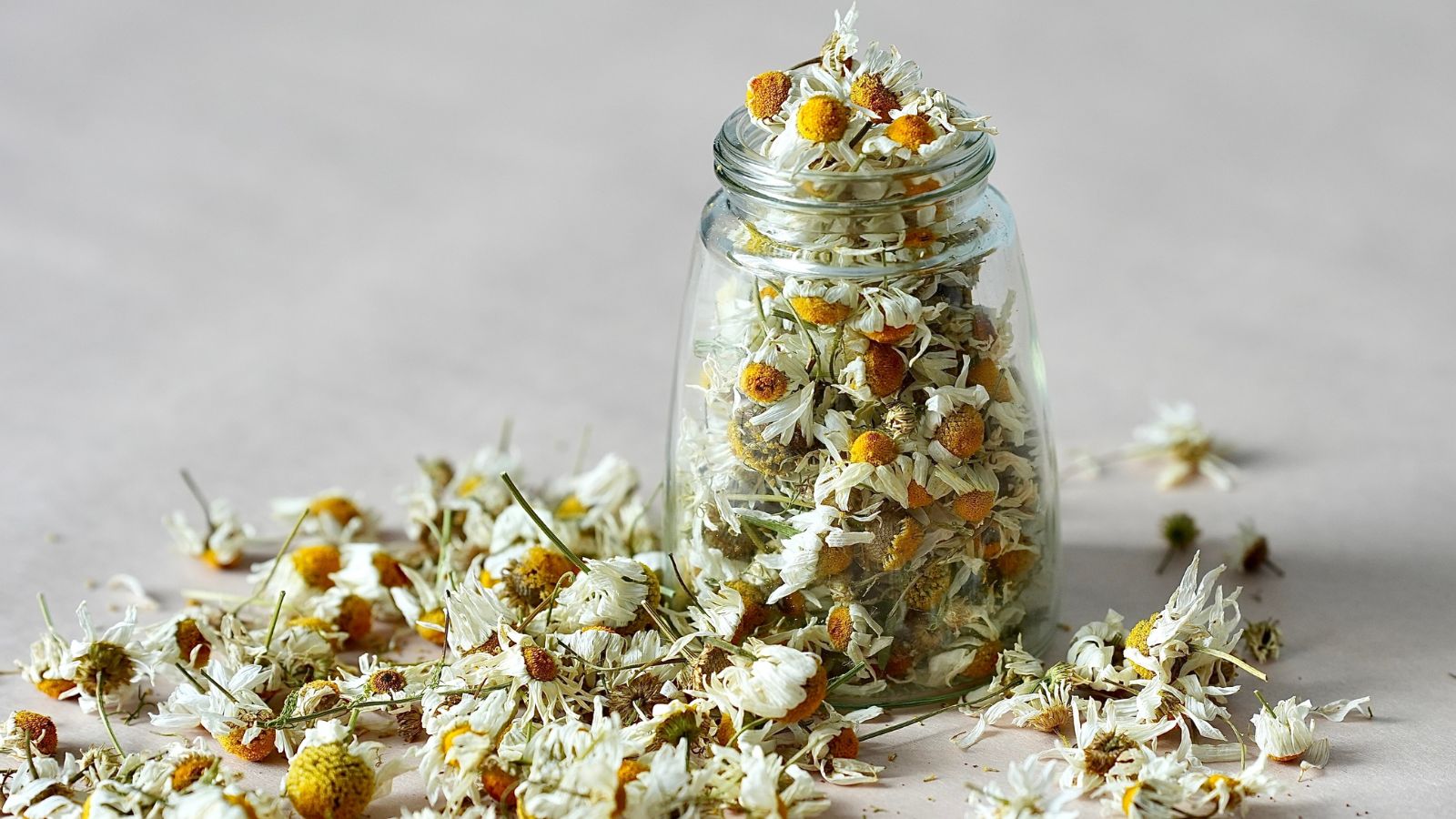 A shot of a jar with dried flowers alongside a pile dried flowers