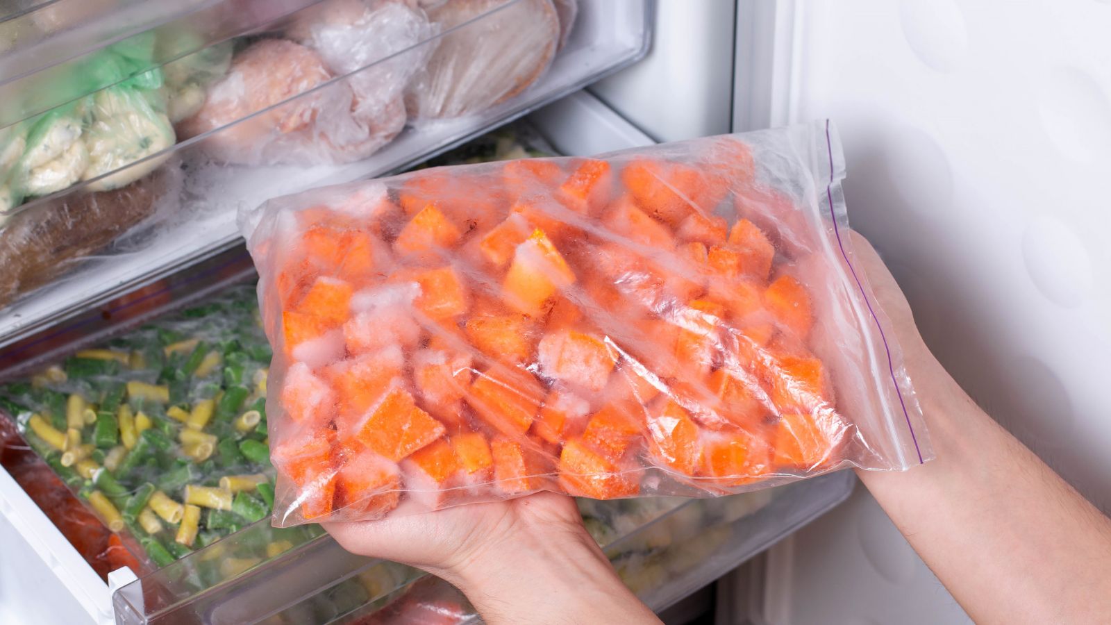 A shot of a person holding a plastic bag of frozen crops taken from a freeer