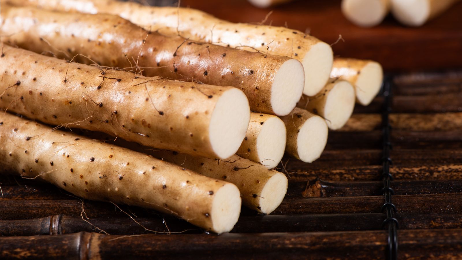 A pile of freshly cit Chinese Yams appearing to have long forms with white insides placed on a dark wooden surface