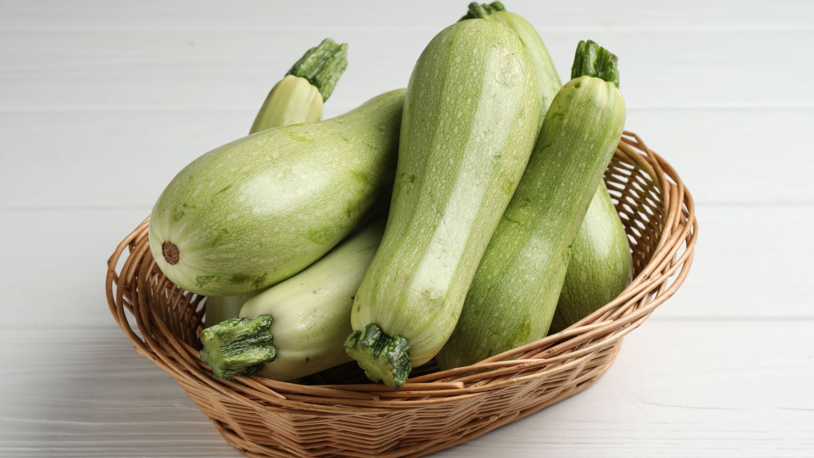 Green summer gourds on a wicker basket in a well lit area indoors