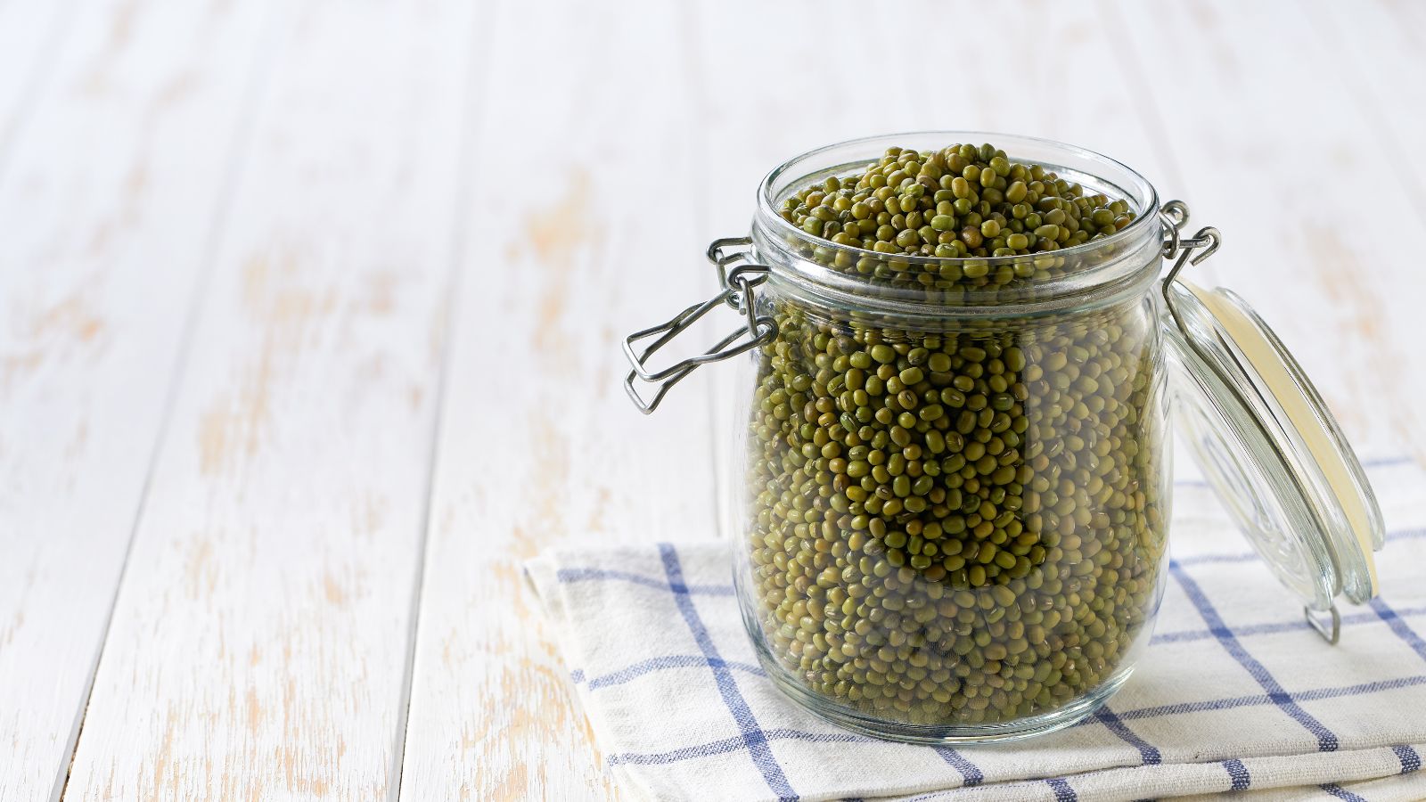 A close-up shot of a jar filled to the brim with harvested legumes, placed on top of a wooden surface indoors