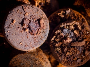 A close-up of brown circular discs, showing their rough and compacted texture, with tiny grains scattered on the surface, creating a rich, earthy appearance, while the background reveals more of these stacked discs.