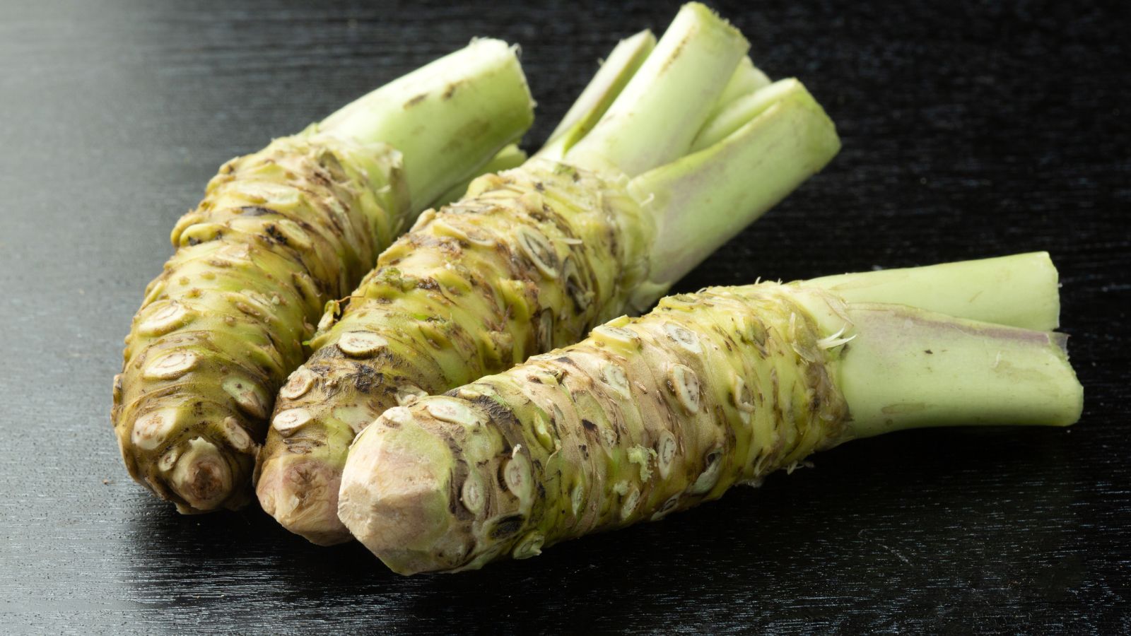 A shot of three root crops placed on a black surface, appearing textured under the light